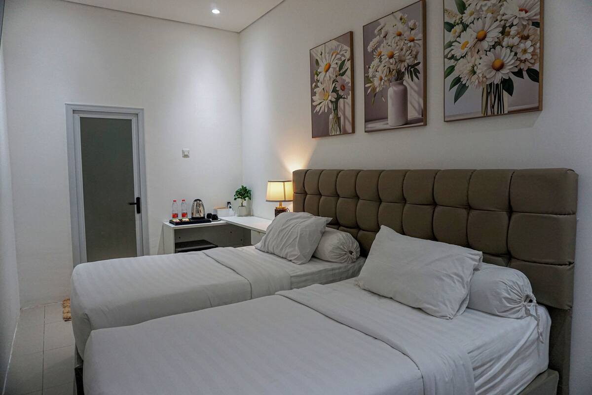 Ein Hotelzimmer mit zwei Betten, einem Schreibtisch und einem Stuhl. An der Wand hängen drei Bilder.