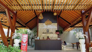 Un área de recepción con techo de madera, pared de mármol con el nombre del hotel y mostrador de recepción.