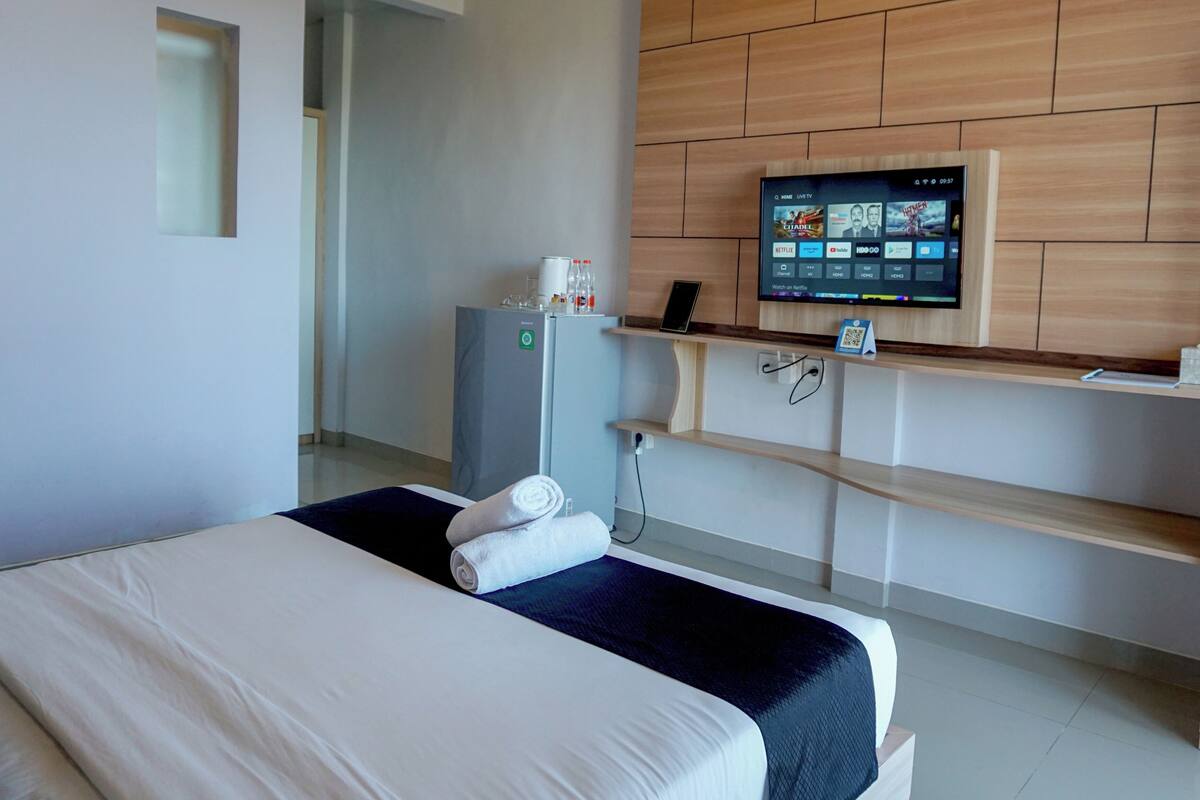 Ein Hotelzimmer mit Bett, Wandfernseher, kleinem Kühlschrank und einer Ablage mit Kaffeemaschine.