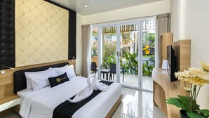 Habitación de hotel con una cama grande, un escritorio de madera, televisión y vistas a un jardín a través de la puerta corrediza de vidrio.