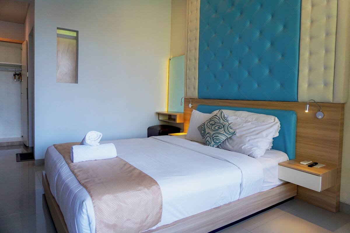 Ein modernes Hotelzimmer mit einem großen Bett, einem Holfnachtkästchen und einem blauen Kopfteil.