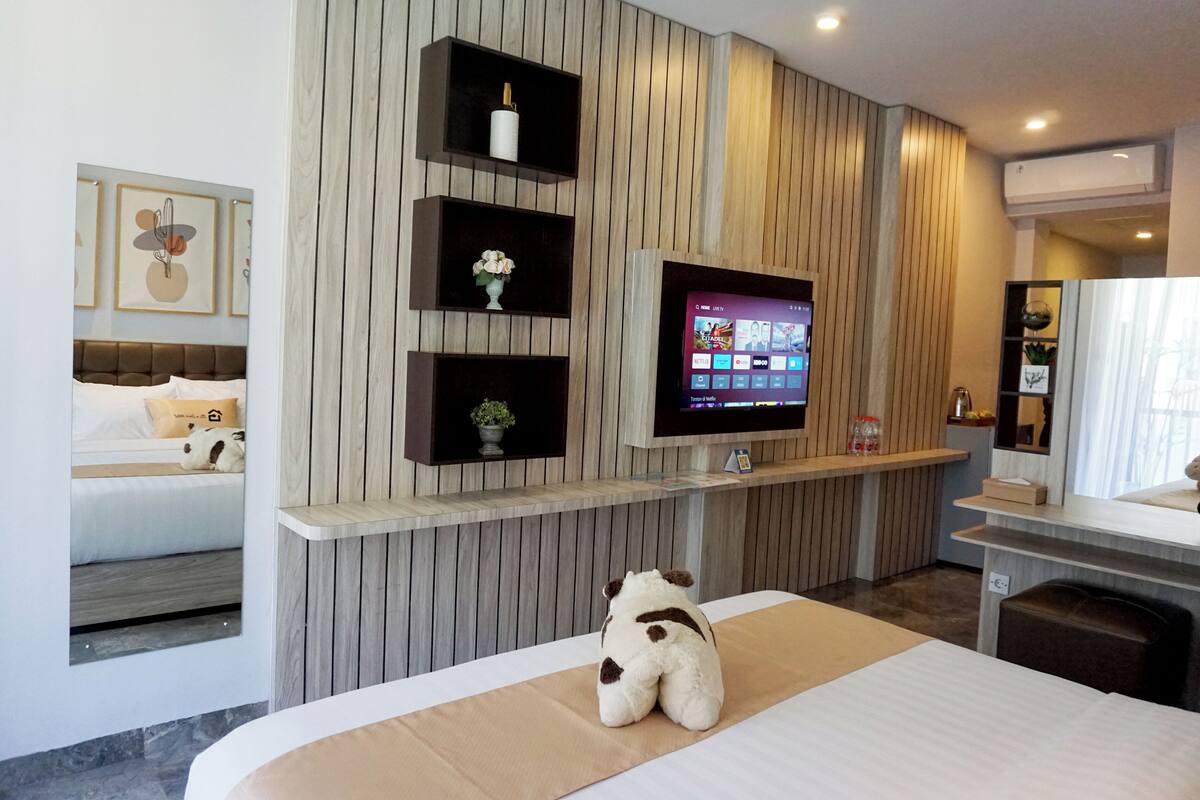 Ein Hotelzimmer mit einem Bett, einem an der Wand montierten Fernseher, einer kleinen Ablage mit Dekoration und einem Stofftier auf dem Bett.