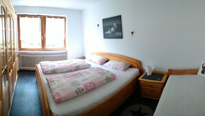 Une chambre à coucher comprenant un lit, une table de chevet, une commode, un radiateur et une fenêtre.