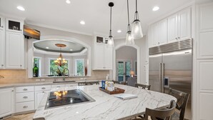 A spacious kitchen with white cabinetry, a large marble island, stainless steel appliances, and pendant lighting.