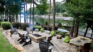 A patio with Adirondack chairs, a fire pit, and a view of a lake.