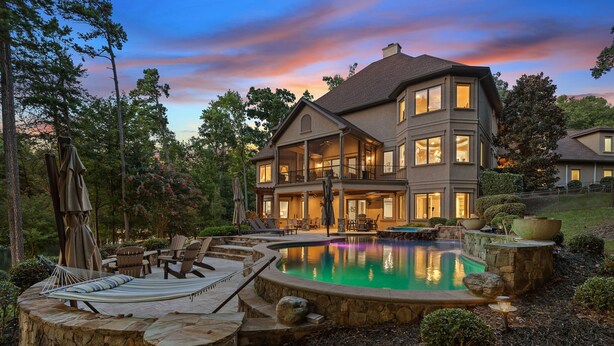 A large, two-story house with a swimming pool, outdoor seating, and a well-maintained garden.