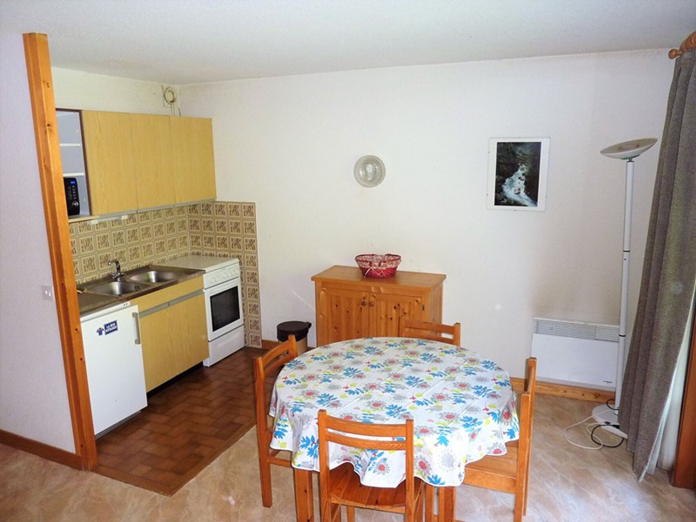 Una cucina compatta con lavello, fornello e pensili in legno. Un piccolo tavolo con sedie si trova al centro.