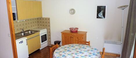 Una cucina compatta con lavello, fornello e pensili in legno. Un piccolo tavolo con sedie si trova al centro.