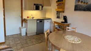 Een kleine keuken met een vaatwasser, een magnetron en een koffiezetapparaat op een houten tafel.