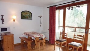 A cozy room with a wooden table and benches, a small cabinet, a painting on the wall, and a window with curtains. - Studio 28m² with pool, balcony, parking - St-Jean-d'Aulps (Saint-Jean-d'Aulps)
