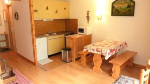 A compact kitchen with a microwave, sink, and wooden cabinets. There's a small dining area with a bench and a table, and a wall-mounted picture of a countryside scene. - Studio 28m² with pool, balcony, parking - St-Jean-d'Aulps (Saint-Jean-d'Aulps)