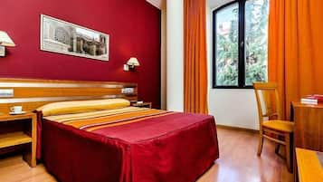 Una habitación de hotel con una cama grande, un escritorio, una silla y un ventanal con cortinas.