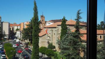 A street view with parked cars, a building with a tower, and trees.