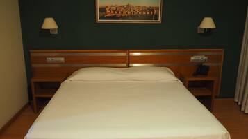 Habitación de hotel con una cama individual, dos mesitas de noche, una mesita con teléfono y un cuadro enmarcado en la pared.