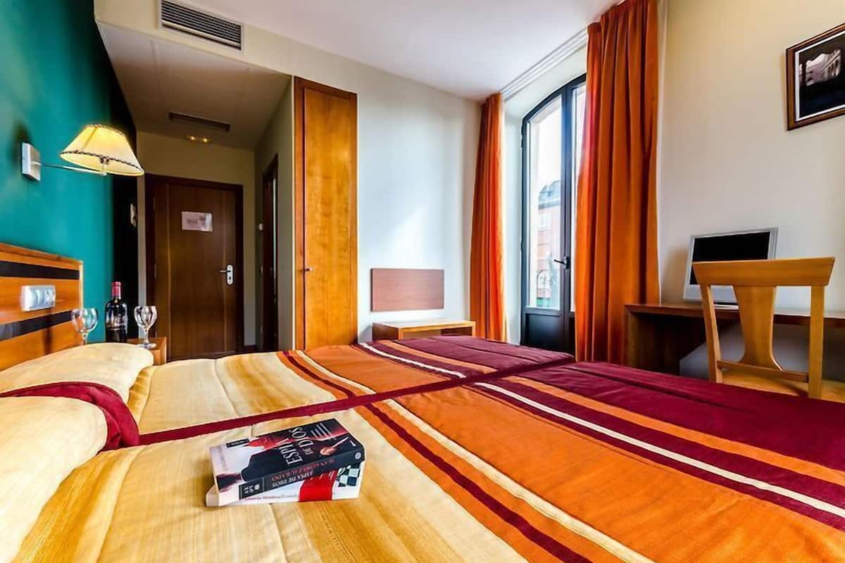 Ein Hotelzimmer mit einem großen Bett, einem Schreibtisch, einem Sessel, einem Fernseher und einem Fenster mit Vorhängen.