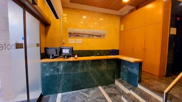 A reception desk with two monitors, a framed picture on the wall, and a yellow wall with a 'SALIDA' sign.
