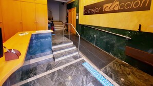 A hotel lobby with a reception desk, a staircase with a handrail, and a sign that reads "su mejor elección". - ELE Mirador de Santa Ana (Ávila)