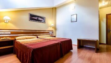 A hotel room with a double bed, bedside tables, a small bench, and wall-mounted lamps.
