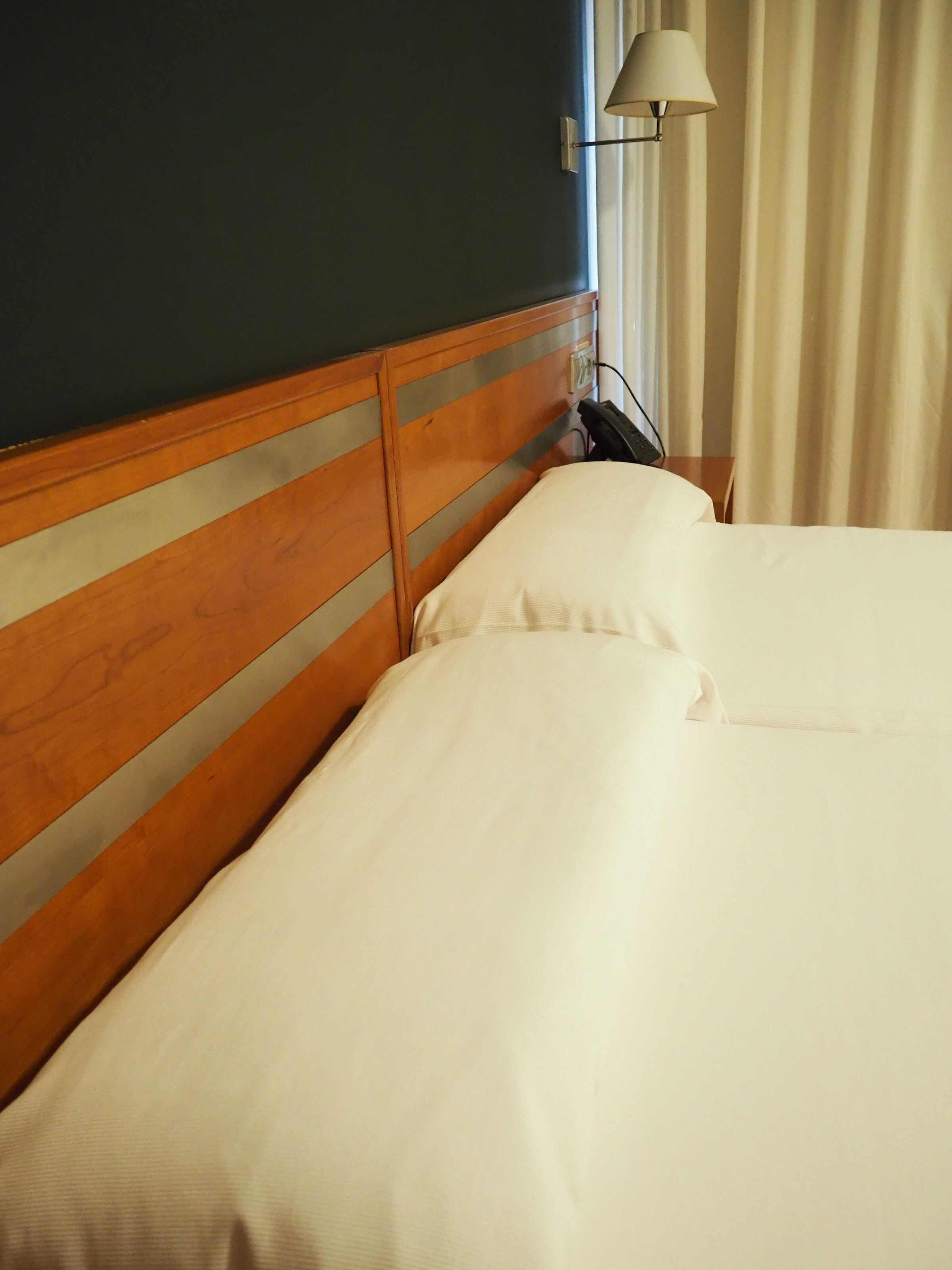 Una cama bien hecha con ropa de cama blanca en una habitación con cabecera de madera y una lámpara en una mesita de noche.
