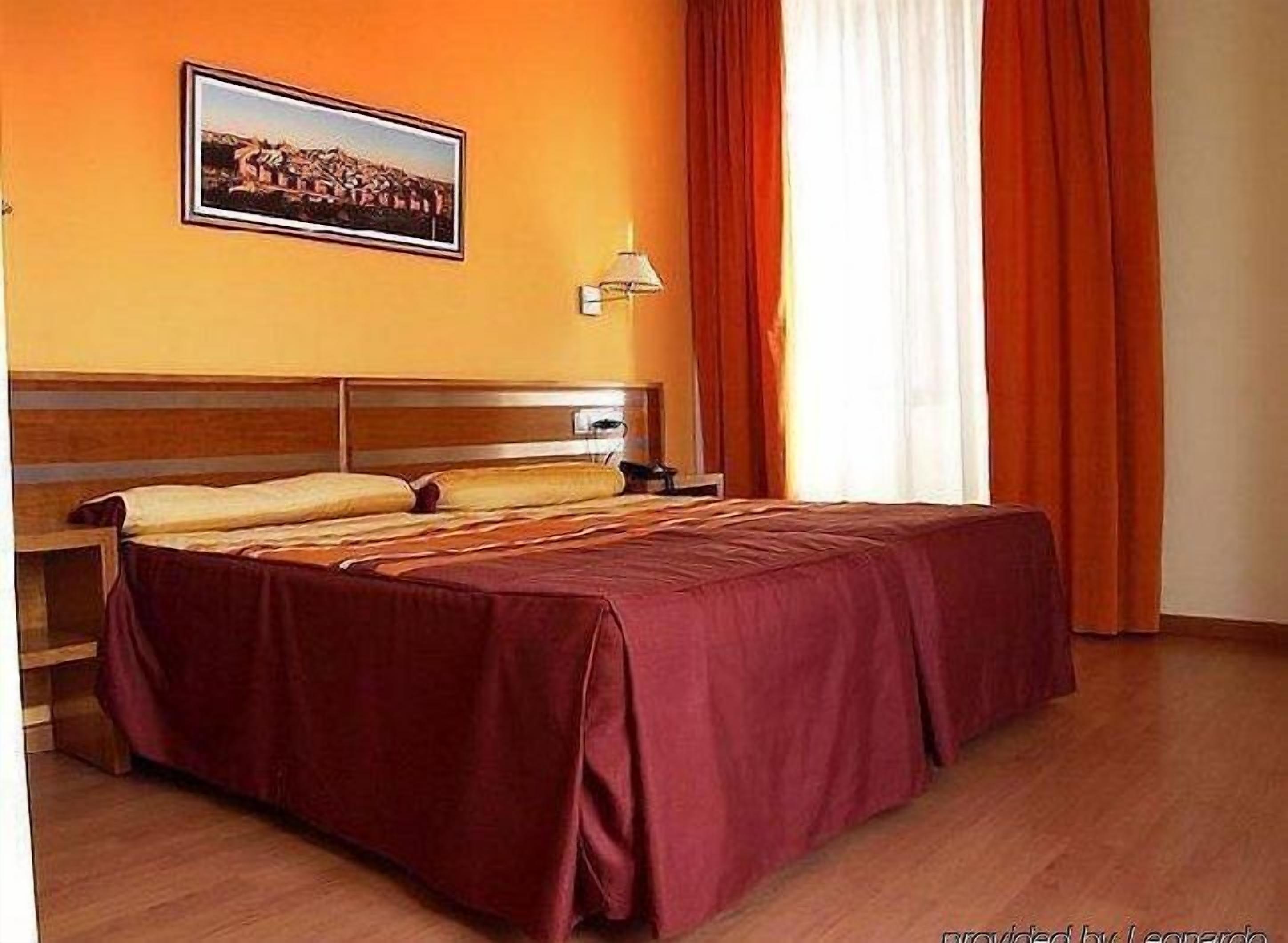 Habitación de hotel con una cama de madera, una mesita de noche, una lámpara y un cuadro en la pared.