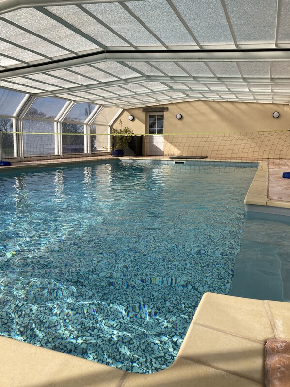 Una piscina interior con agua cristalina, estructura de techo y pared color beige.