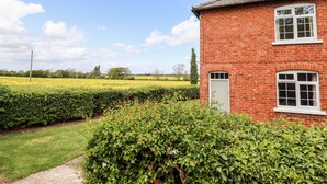 A brick house with a white door and windows, surrounded by a well-maintained garden and a field in the background. - East Farm Cottage (Lincoln)