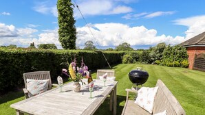 A wooden table with chairs, a vase of flowers, a bottle of wine, and a barbecue grill in a garden setting. - East Farm Cottage (Lincoln)