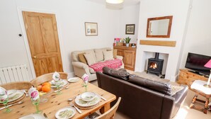 A cozy living room with a wooden dining table set for four, a brown leather sofa, a fireplace, and a television on a wooden stand. - East Farm Cottage (Lincoln)