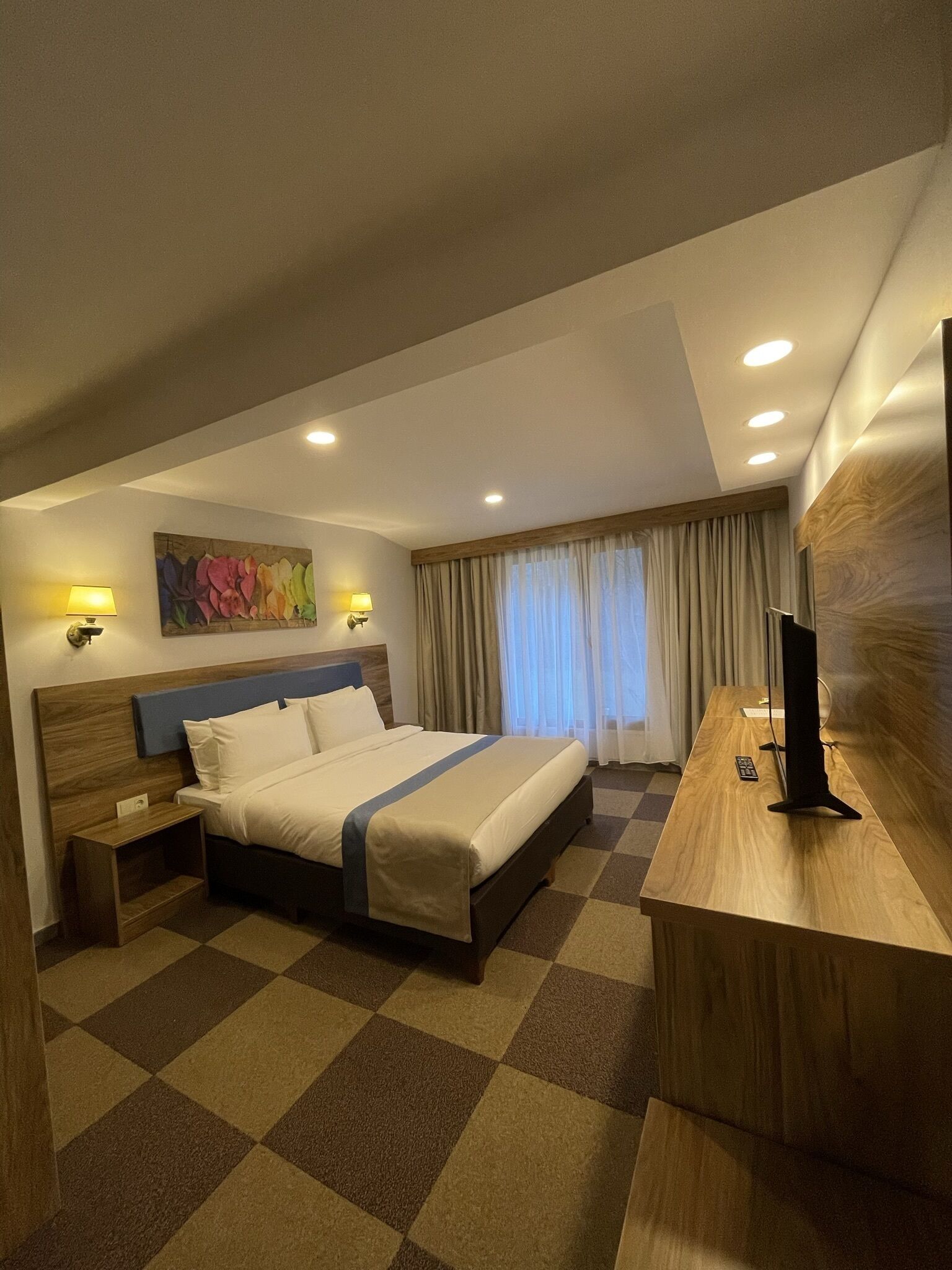 Een hotelkamer met een groot bed, een bureau, een televisie en een schilderij aan de muur.