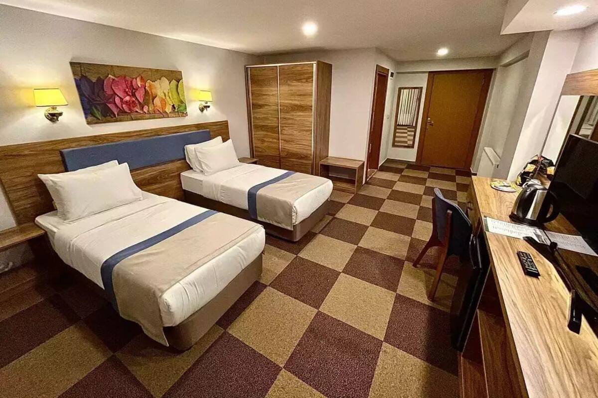 Een hotelkamer met twee bedden, een bureau, een televisie en een schilderij aan de muur.