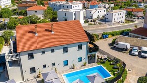 En bostadsbyggnad med ett rött tegeltak, en swimmingpool och en parkeringsplats med flera fordon.