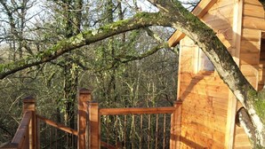 Eine Holzhütte mit einer Holzterrasse und einem Metallgeländer, umgeben von Bäumen.