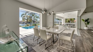 A spacious dining area with a large table and chairs, a glass coffee table, and pendant lighting. - Villa Inspiration - modern style, spectacular view, large pool area  (Cape Coral)