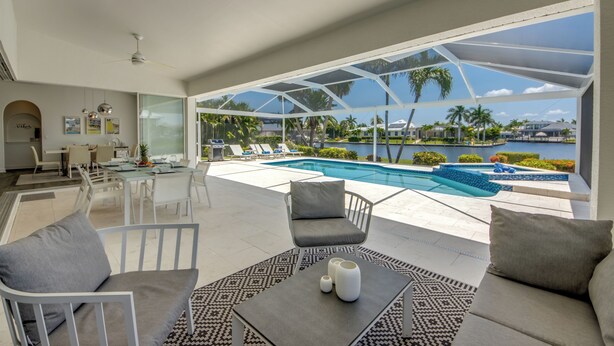 A modern living room with a pool view, white furniture, and a dining area. - Villa Inspiration - modern style, spectacular view, large pool area  (Cape Coral)