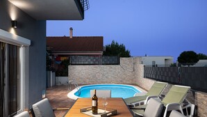 An outdoor pool area with a wooden table and lounge chairs, a stone wall, and a metal fence. - Villa Papillon – lovingly furnished & superbly equipped vacation oasis with pool (Pula)