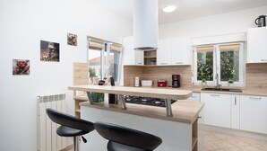 A modern kitchen with white cabinets, a wooden countertop, and a gas stove. There are two black bar stools in front of the counter. - Villa Papillon – lovingly furnished & superbly equipped vacation oasis with pool (Pula)