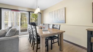 A dining area with a wooden table, chairs, a hanging light fixture, and a large abstract painting on the wall. - Townhouse with Free Shuttle to Tremblant Resort (Mont-Tremblant)