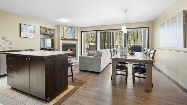 A modern kitchen with a central island, a dining area with a table and chairs, a sofa, and a fireplace. - Townhouse with Free Shuttle to Tremblant Resort (Mont-Tremblant)