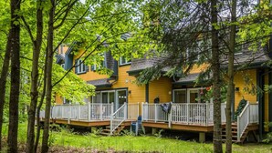 A yellow building with multiple decks and a covered porch, surrounded by trees. - Townhouse with Free Shuttle to Tremblant Resort (Mont-Tremblant)