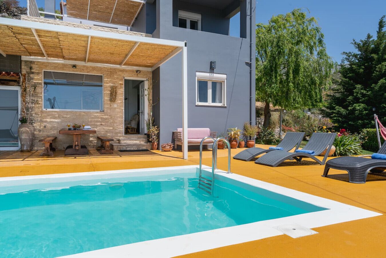 A swimming pool with lounge chairs, a covered patio, and a building with a stone facade.