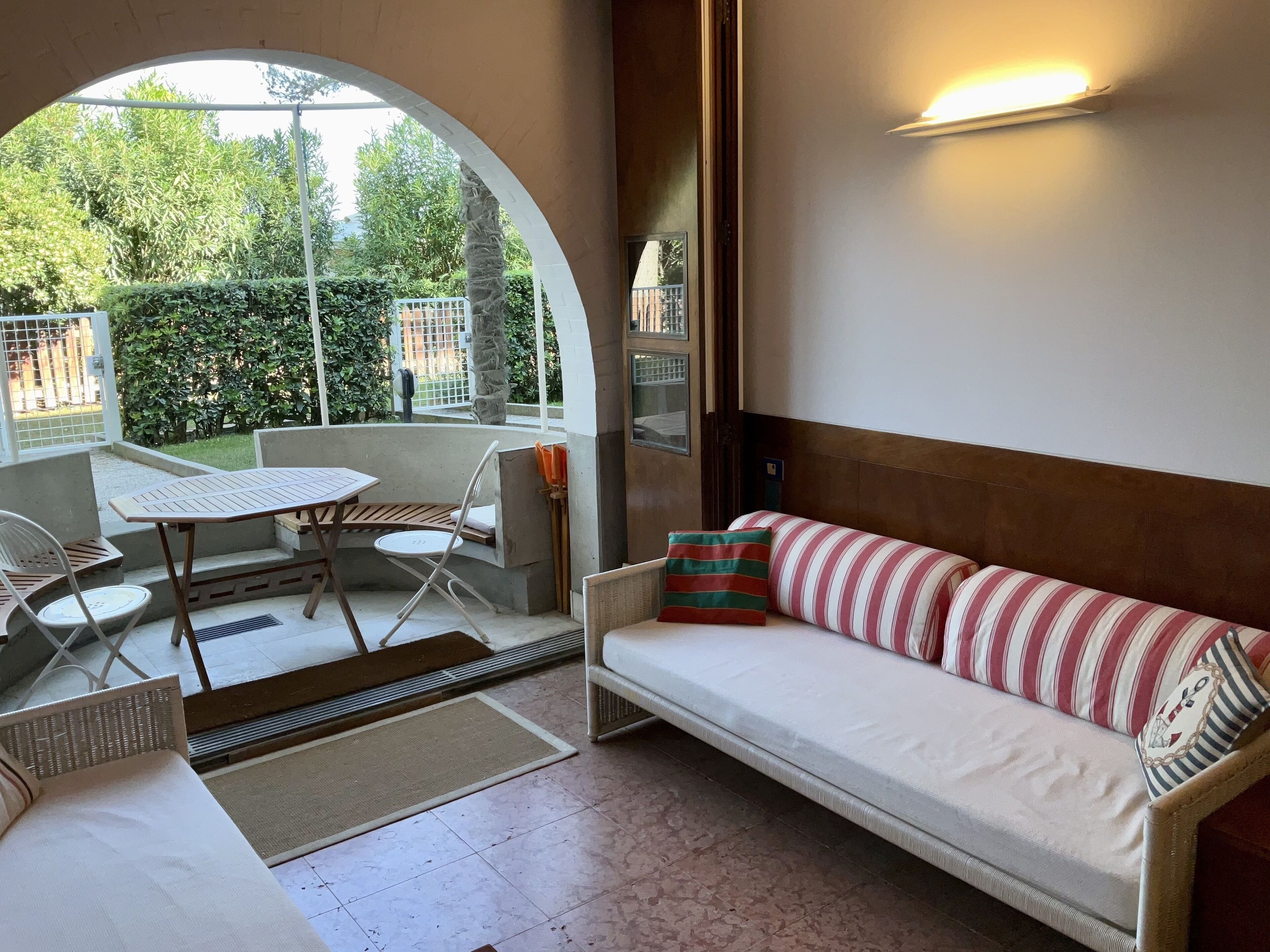 Ein gemütlicher Außenbereich mit einer Sitzecke, inklusive Sofa und Sesseln, einem Tisch und Blick auf einen Garten.