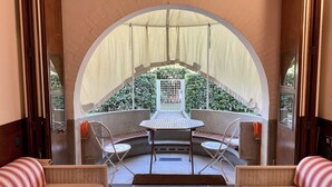 Ein Zimmer mit Blick durch ein rundes Fenster, ein Tisch mit Stühlen und zwei Betten mit gestreiften Kissen.
