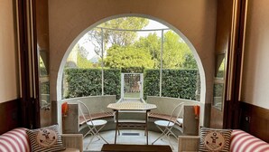 Ein gemütlicher Sitzbereich mit Tisch und Stühlen, ein rundbogiges Durchgangstor und Blick auf einen Garten.