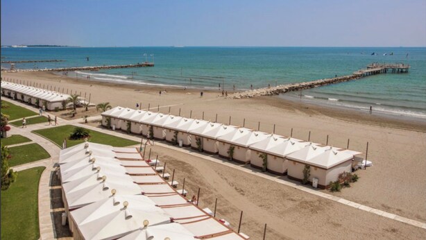 Ein Strandhotel mit Reihen weißer Zelte, einem Sandstrand und einem Pier, der ins Meer ragt.