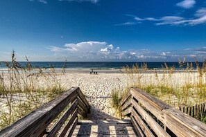 En träpromenad som leder till en sandstrand med en klarblå himmel.