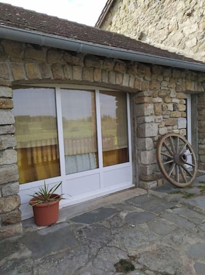A stone building with a large window, a potted plant, and a wooden wheel.