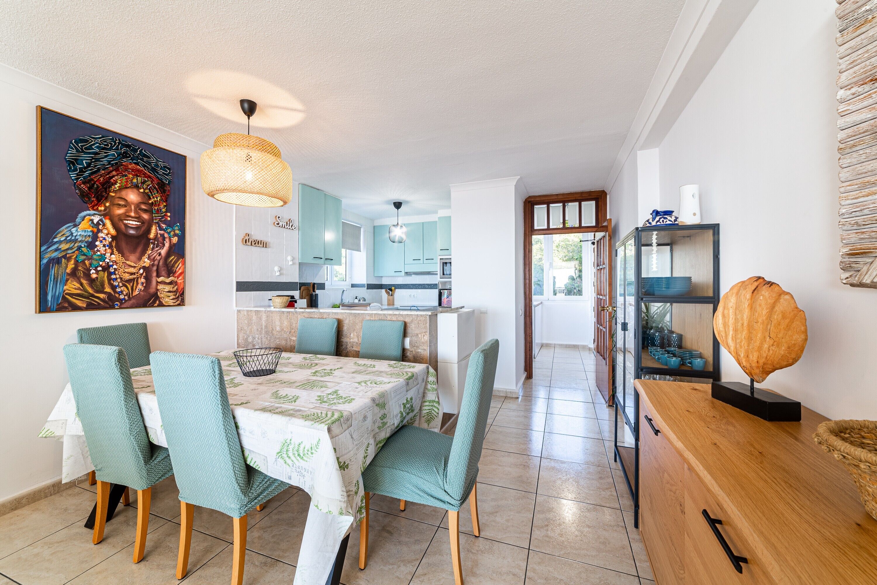 A dining area with a table set for four, a kitchen in the background, and a decorative piece on a console table.