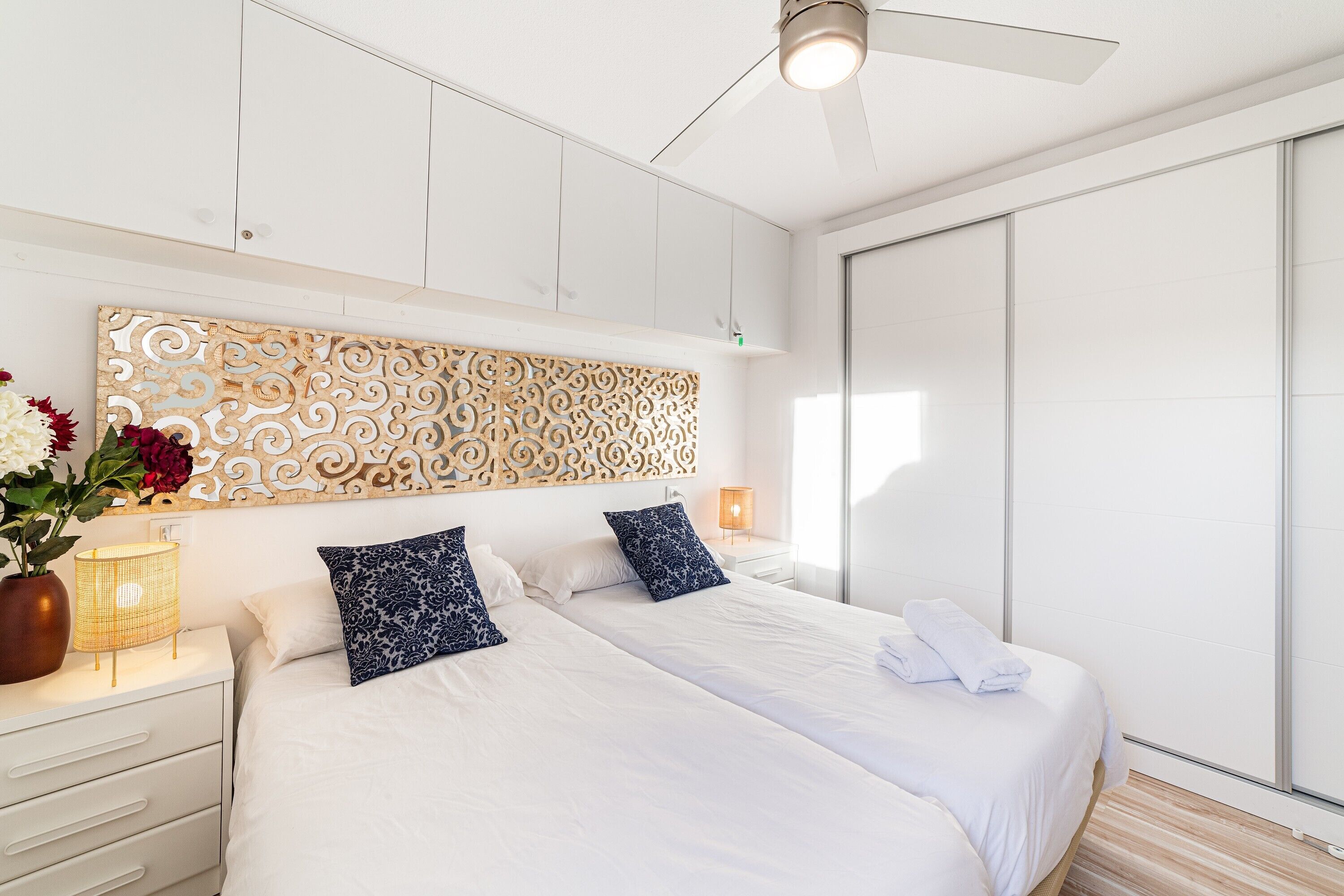 Una moderna camera d'albergo con due letti, un pannello decorativo, un comodino con lampada e un'ampia finestra.