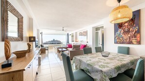 Un vaste espace de vie comprenant une table à manger, des chaises, un canapé et une grande fenêtre donnant sur un paysage agréable.