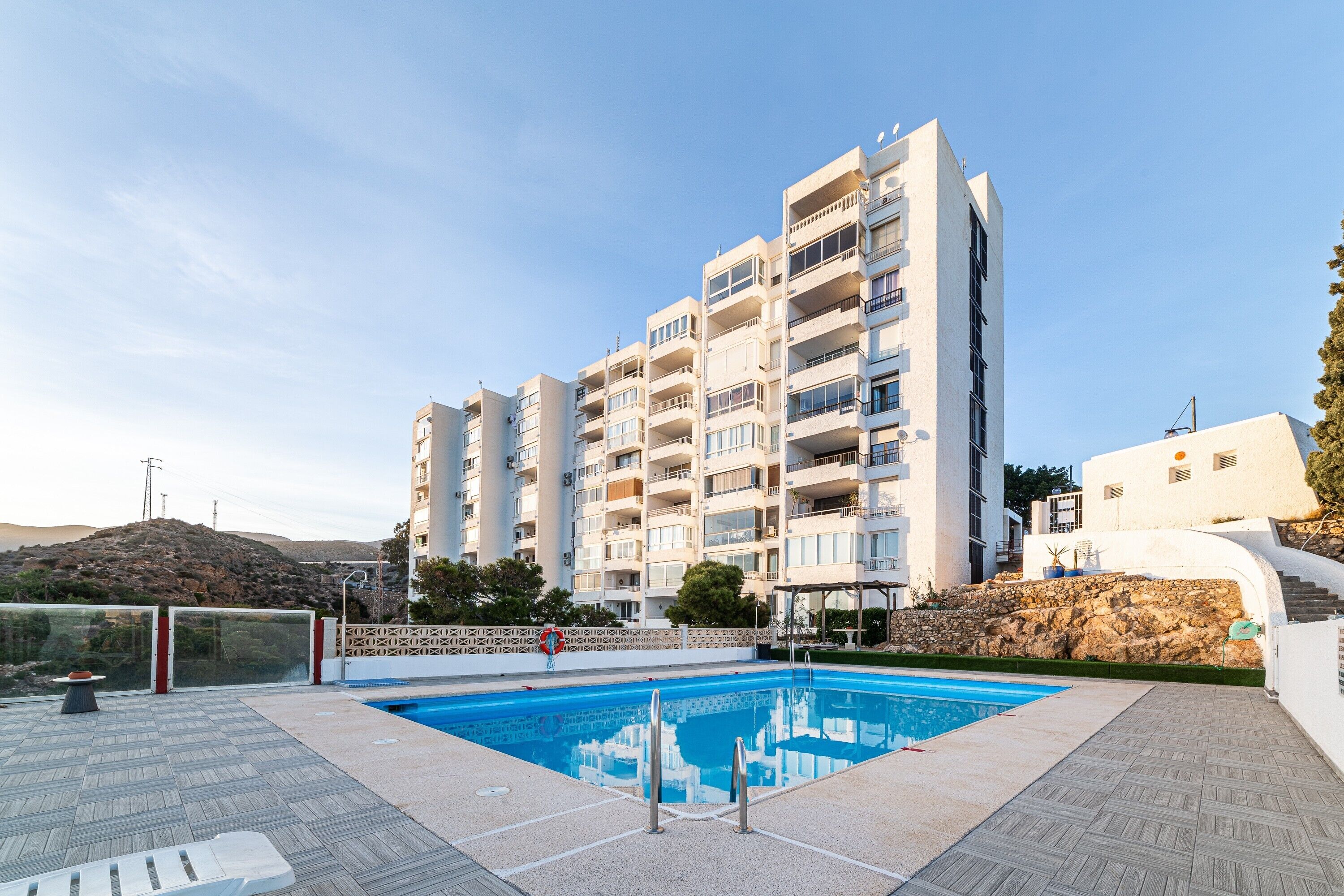 Ein modernes Apartmenthaus mit Schwimmbad, Balkonen und einer Steinmauer.